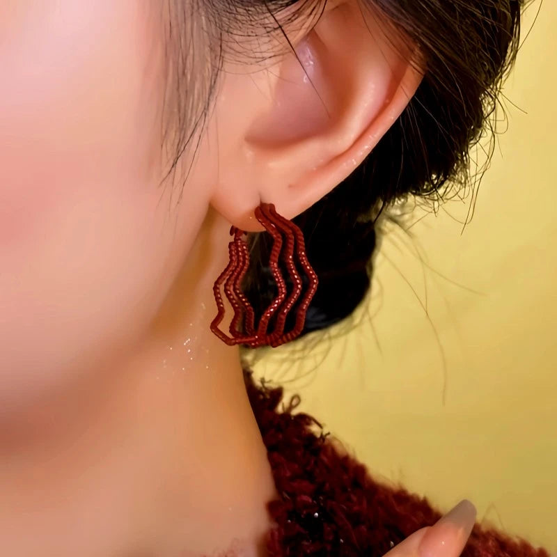 Model showcasing the dangle and style of the 14K Gold-Plated Red Wavy Three-Layer Hoop Earrings