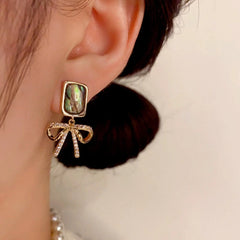 Model showcasing the dangle and style of the 14K Gold-Plated Square Colored Shell Zircon Bow Earrings