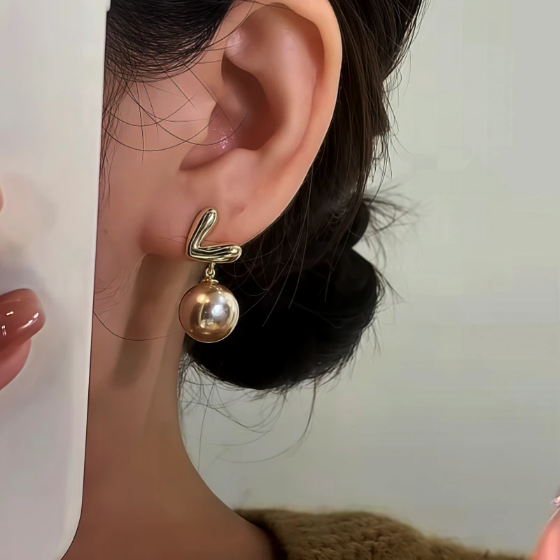 Model showcasing the dangle and style of the 14K Gold-Plated Trendy Heart Pearl Earrings