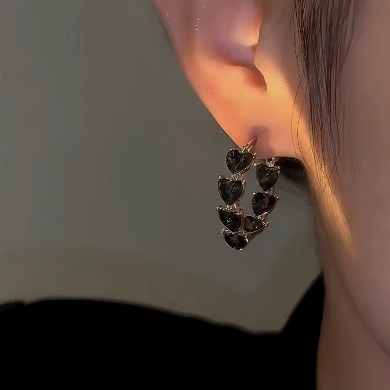Model showcasing the dangle and style of the 14K Gold-Plated Zircon Black Heart Hoop Earrings