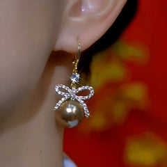 Model showcasing the dangle and style of the 14K Gold-Plated Zircon Bow Brown Pearl Earrings