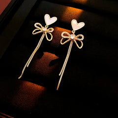 Model showcasing the dangle and style of the 14K Gold-Plated Zircon Bow Heart-Design Tassel Earrings