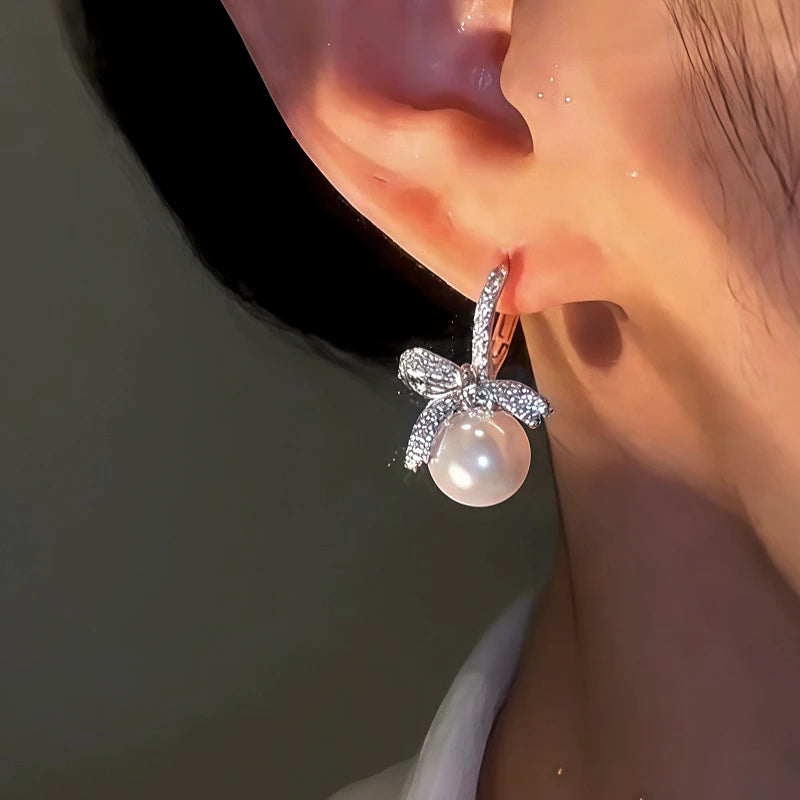 Model showcasing the dangle and style of the 14K Gold-Plated Zircon Bow Pearl Earrings