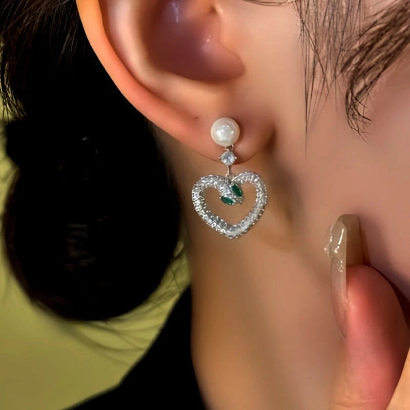 Model showcasing the dangle and style of the 14K Gold-Plated Zircon Green-Eyed Snake Heart Bead Earrings