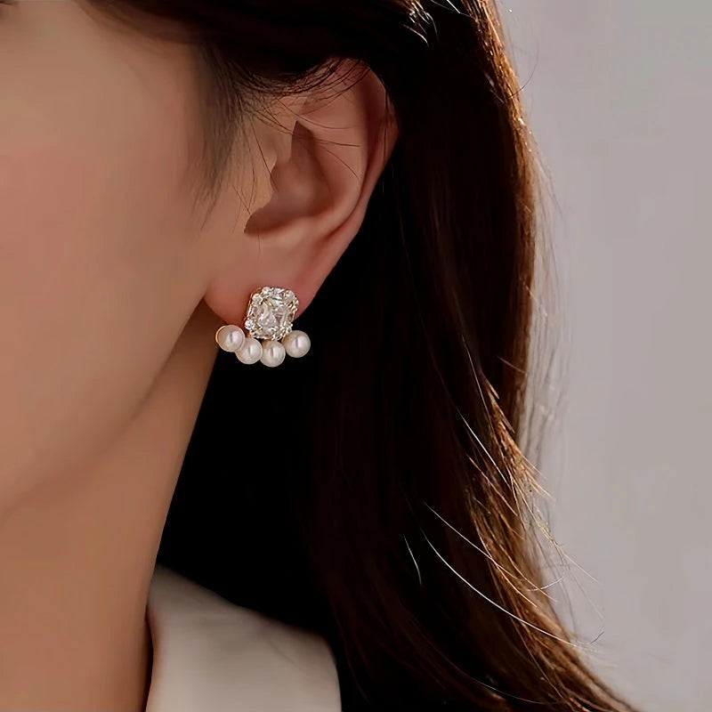 Gold-tone square crystal pearl stud earring worn on a woman's ear