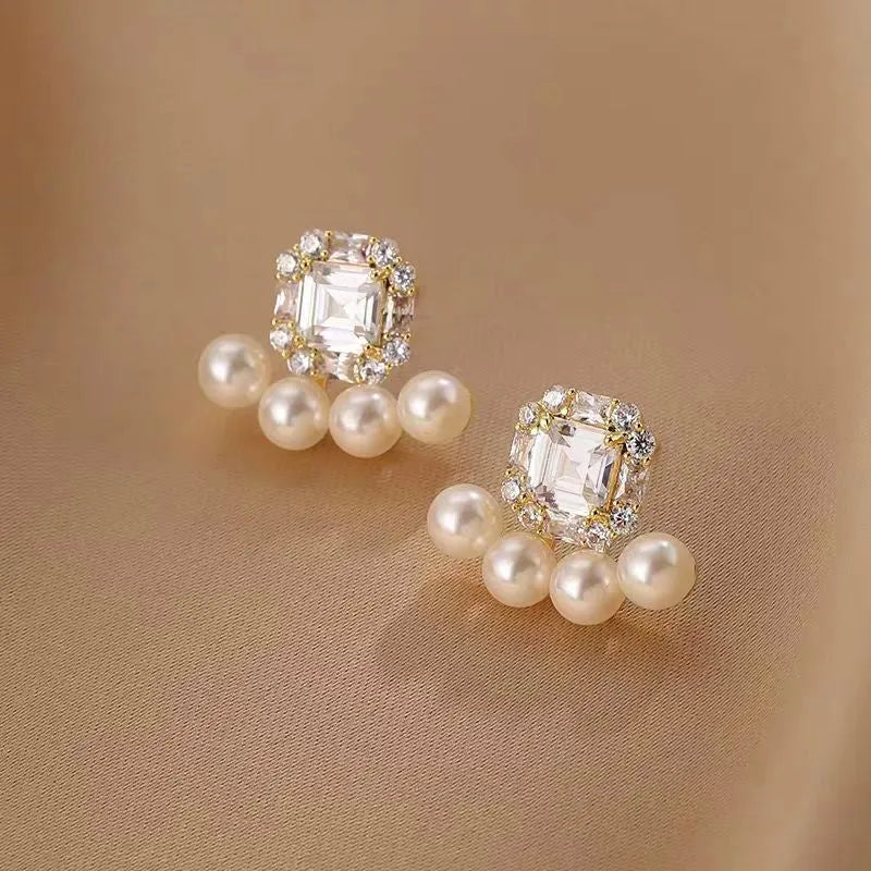 Pair of gold-tone square crystal pearl stud earrings on beige satin fabric