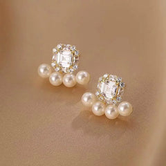 Pair of gold-tone square crystal pearl stud earrings on beige satin fabric