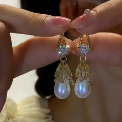 Pair of gold leaf teardrop pearl dangle earrings with cubic zirconia, hand-held closeup