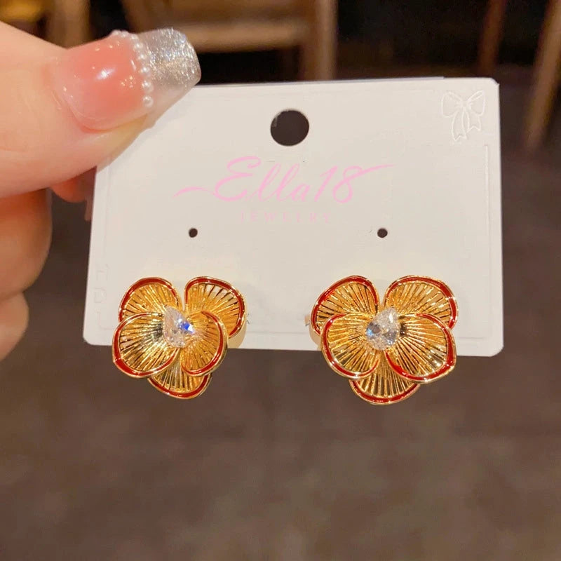 Pair of gold four-petal flower stud earrings: red-edged, ridged petals, teardrop CZ on jewelry card