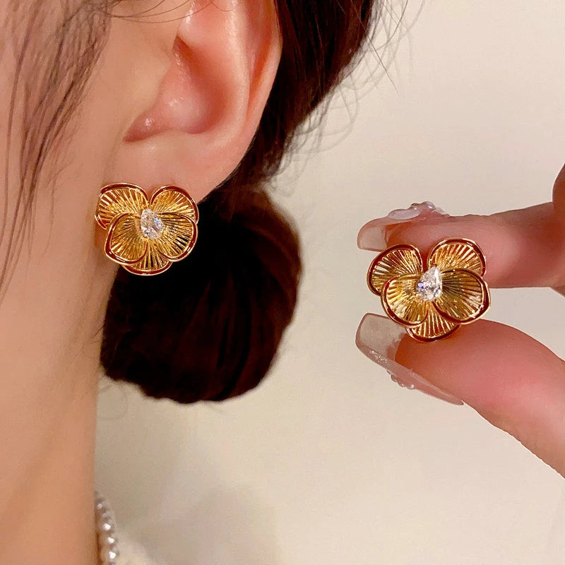 Gold ridged four-petal flower stud earrings with teardrop cubic zirconia, worn and held by hand