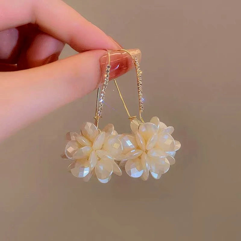 Pair of white flower rhinestone hook dangle earrings held by hand