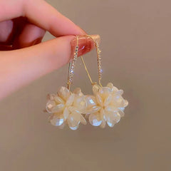 Pair of white flower rhinestone hook dangle earrings held by hand