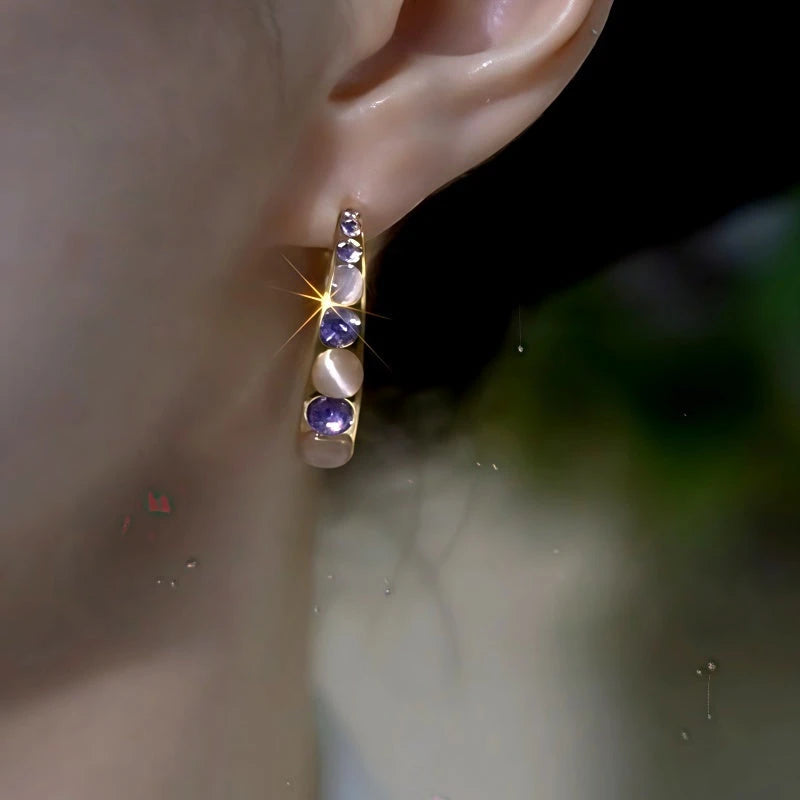 Close-up of gold purple crystal opal half hoop earring worn on woman's ear