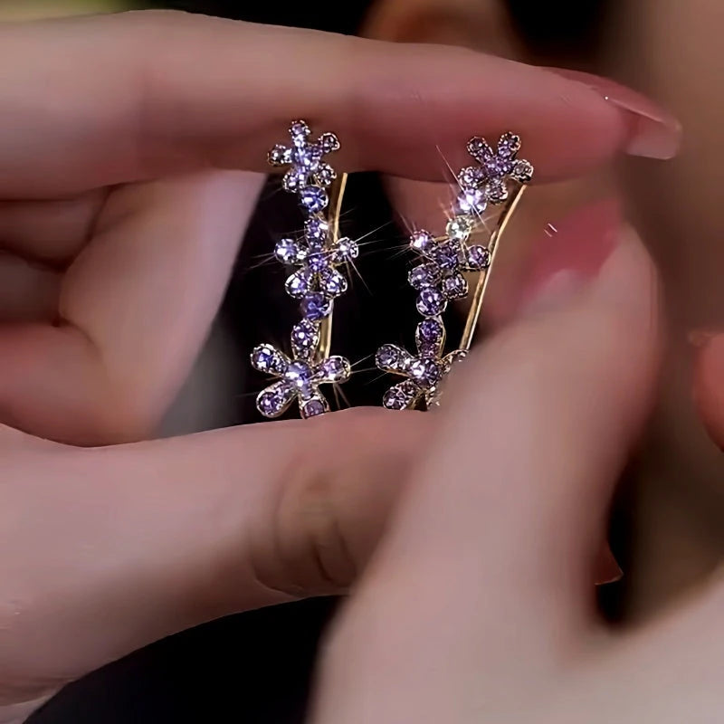 Pair of purple rhinestone flower ear climber earrings held in hand