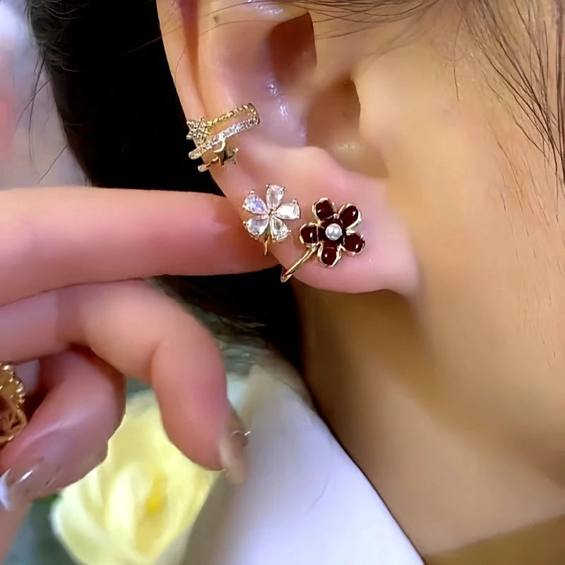 Dual-flower gold earring worn on earlobe with star ear cuff, finger touching ear