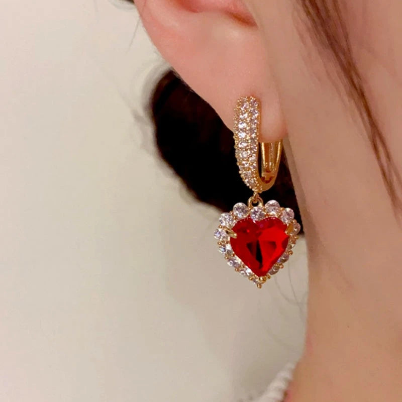 Side view of gold red heart crystal dangle hoop earring on ear