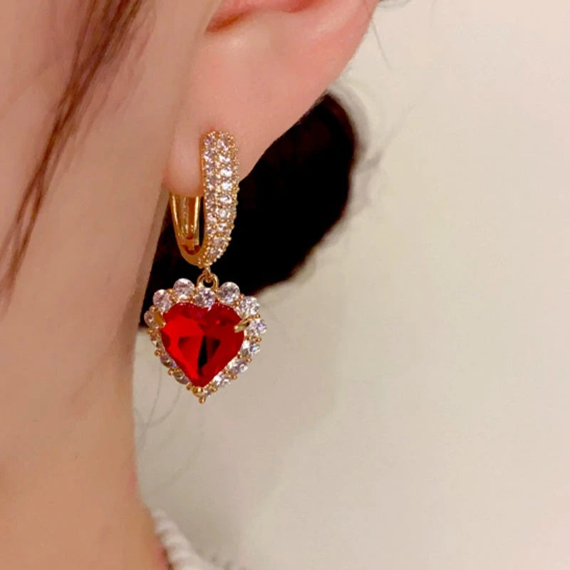 Close-up of gold red heart crystal drop hoop earring worn on ear
