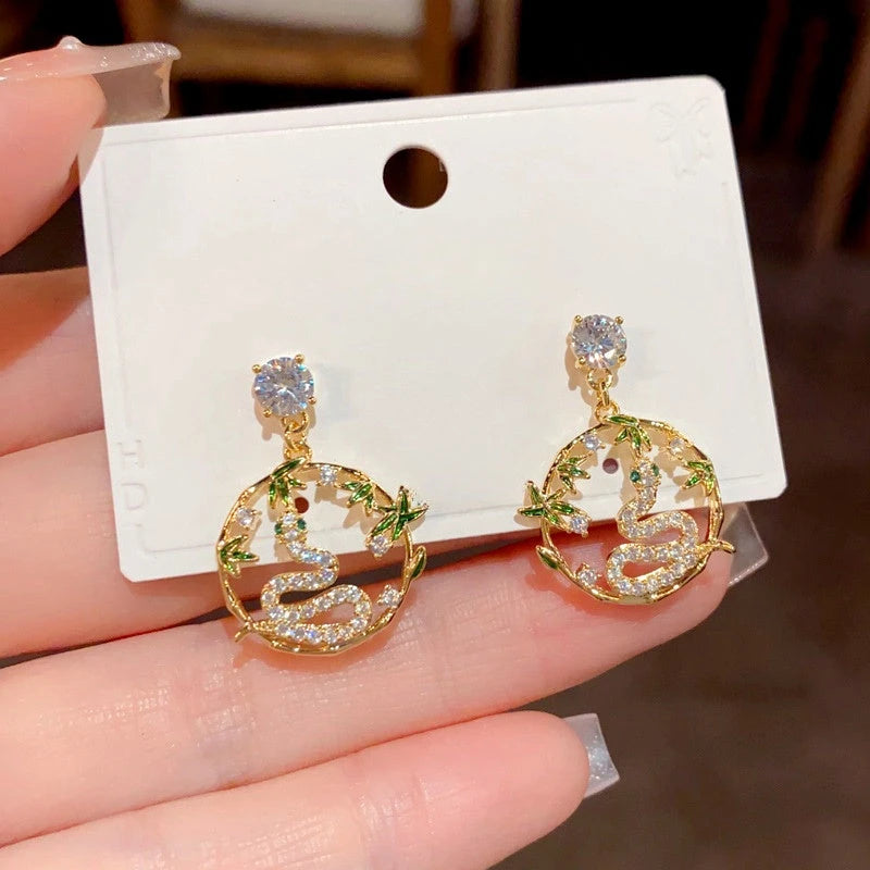 Pair of gold bamboo snake CZ dangle earrings on white jewelry card