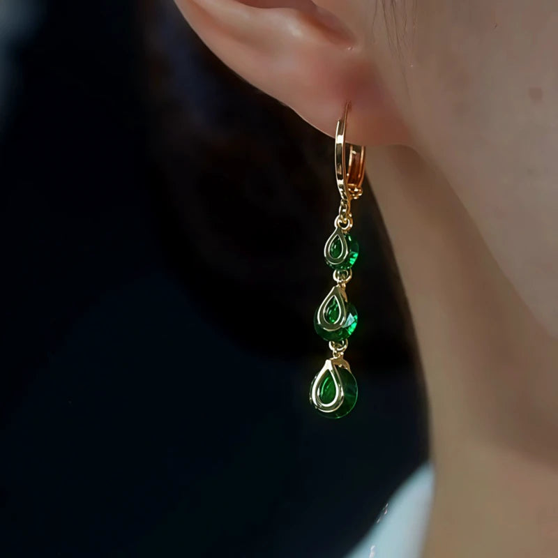 Gold emerald green teardrop dangle hoop earring worn on ear close-up
