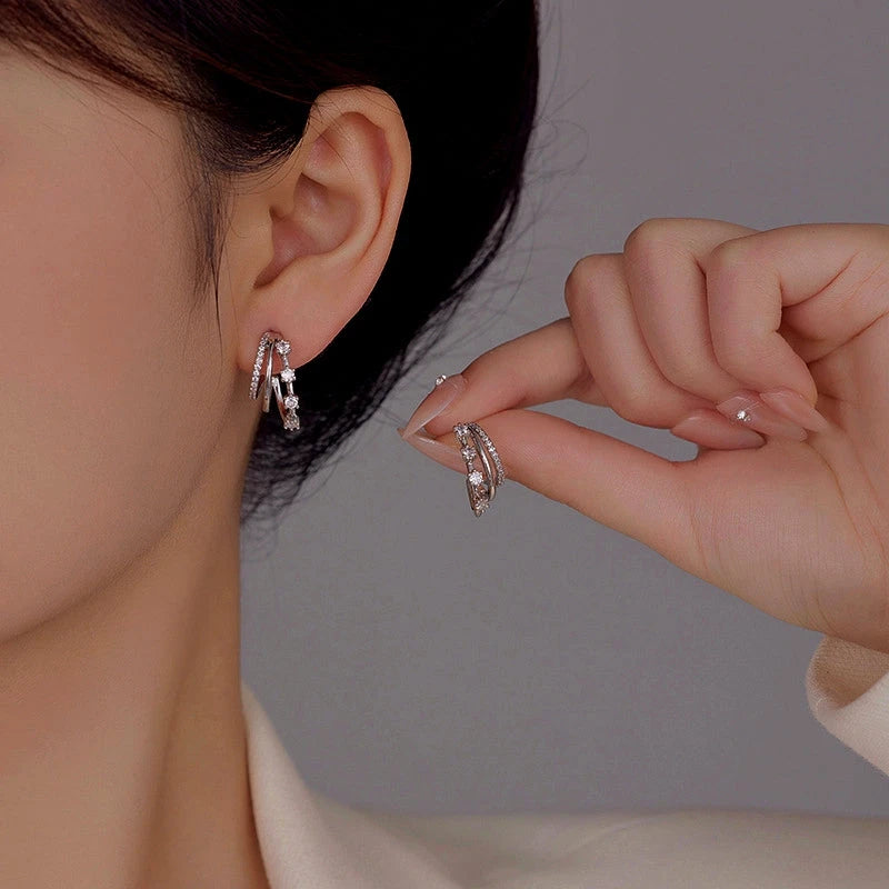 Silver triple-layer CZ hoop stud earrings worn on woman's ear, hand holding matching earring