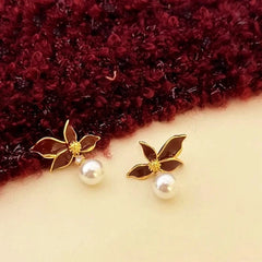 Pair of burgundy enamel flower pearl drop earrings laid flat on fabric background