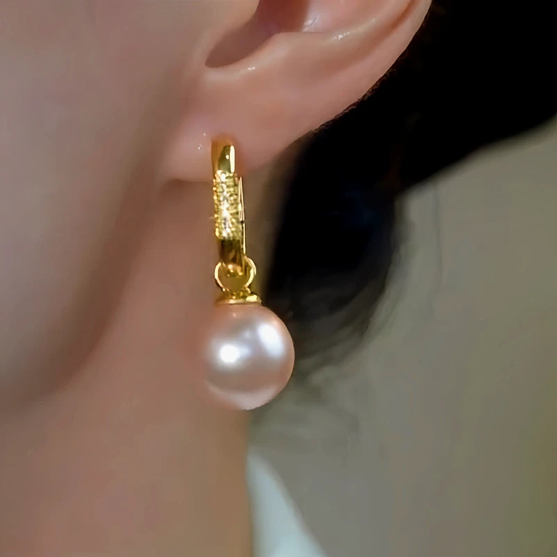 Gold pave pearl drop huggie hoop earring worn on a person's ear