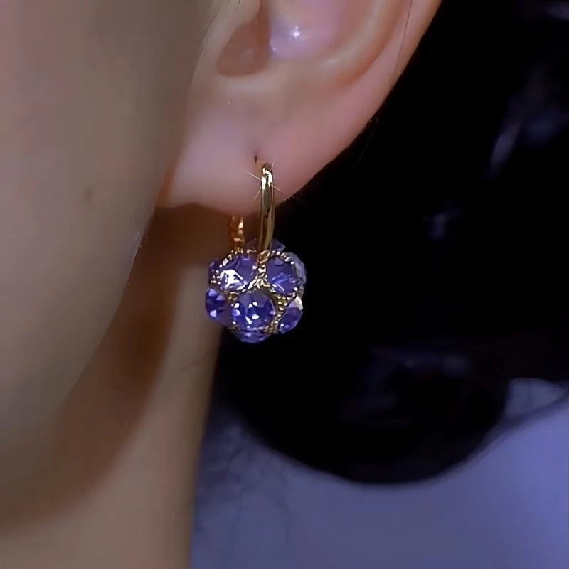Close-up of purple crystal gold huggie earring worn on earlobe