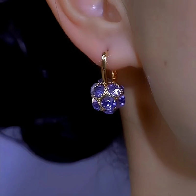 Side view of faceted purple crystal gold hoop earring on earlobe