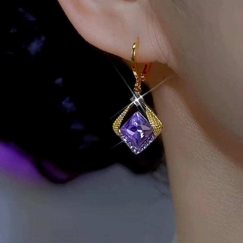 Close up of gold purple square crystal drop earring worn on woman's ear