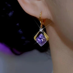 Close up of gold purple square crystal drop earring worn on woman's ear