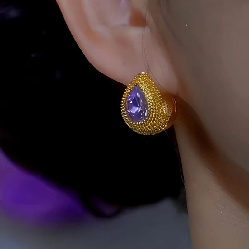 Textured gold teardrop purple gemstone stud earring worn on ear, side close-up