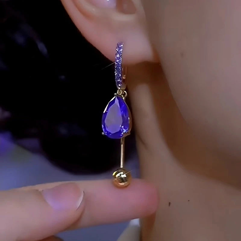 Purple teardrop crystal gold ball dangle hoop earring worn on ear close-up