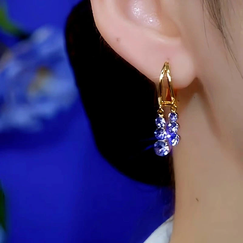Gold teardrop hoop earring with purple-blue crystal dangles worn on ear, close up