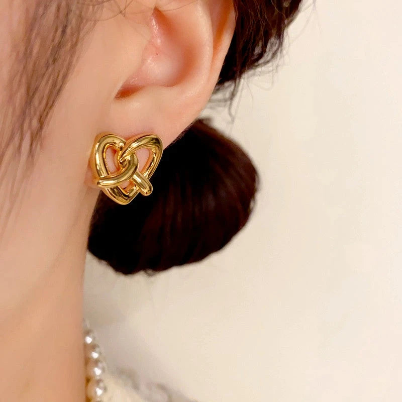 Model showcasing the dangle and style of the 14K Gold Plated Knotted Love Heart Stud Earrings