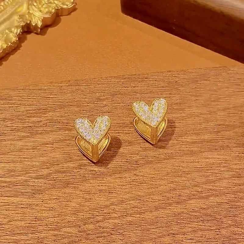 Women's gold pave CZ heart stud earrings on warm wooden surface