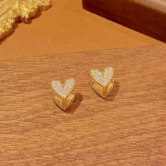 Women's gold pave CZ heart stud earrings on warm wooden surface