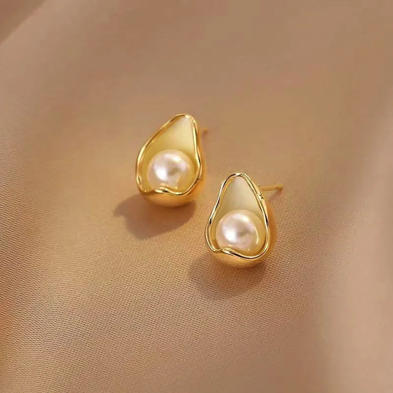 Pair of dainty teardrop gold pearl stud earrings on beige satin