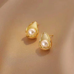 Pair of dainty teardrop gold pearl stud earrings on beige satin