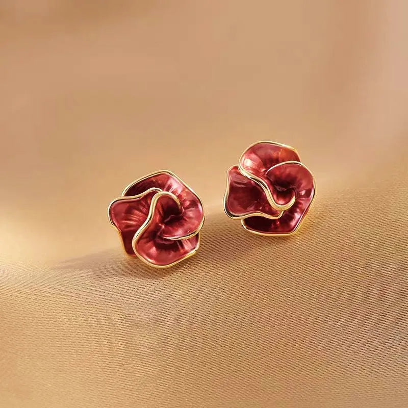 Pair of red rose enamel gold trim stud earrings front view on beige fabric