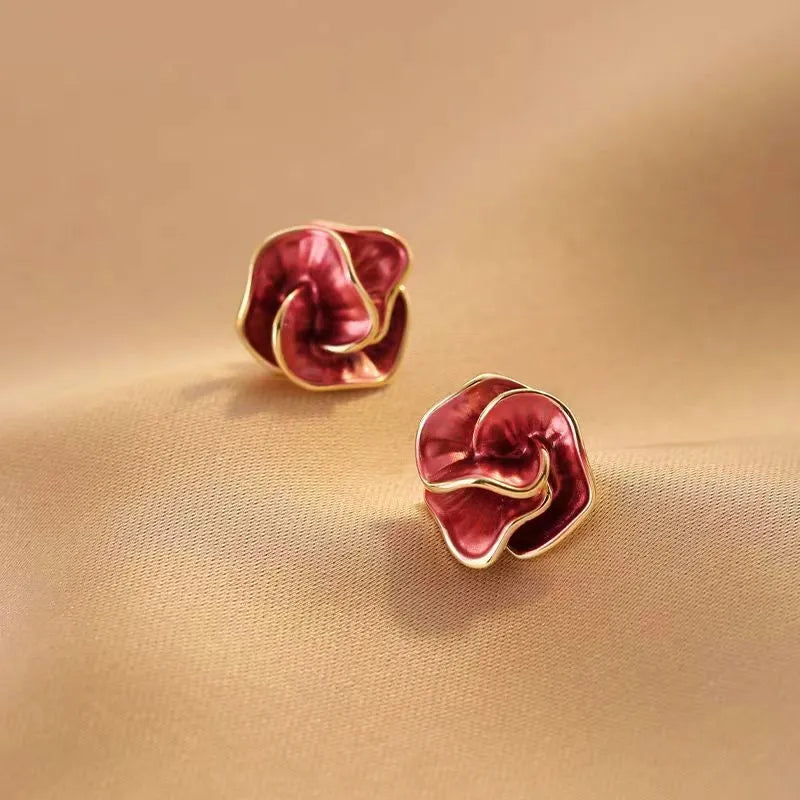 Red rose enamel gold trim stud earrings angled view on beige fabric