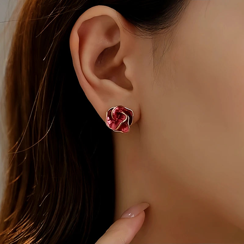 Red enamel rose stud earring with gold trim worn on woman's earlobe