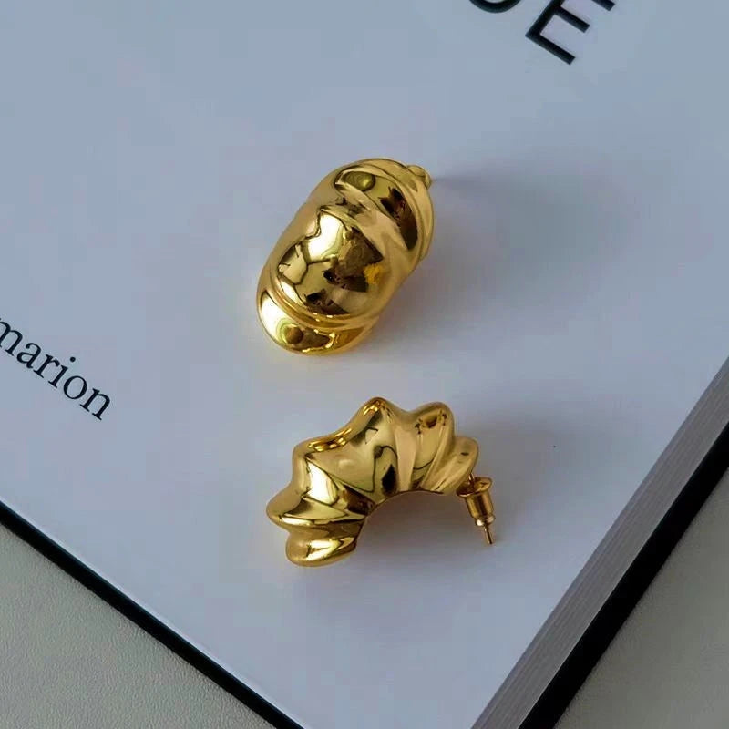 Gold mismatched sculptural ribbed statement hoop earrings on book page