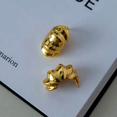 Gold mismatched sculptural ribbed statement hoop earrings on book page