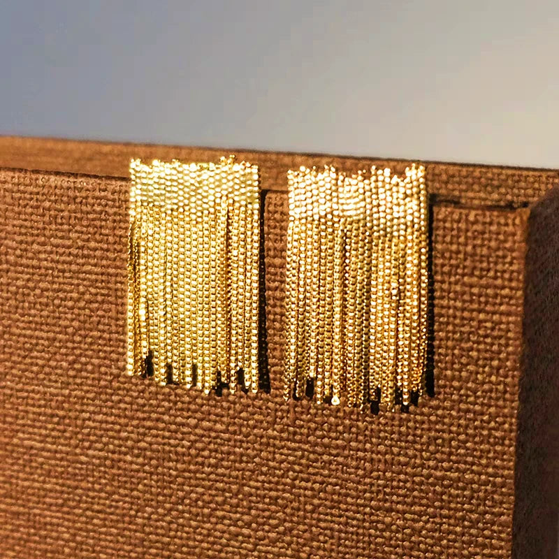 Close-up of gold beaded chain tassel stud earrings on brown textured fabric
