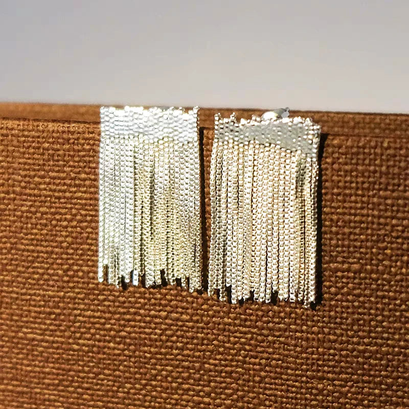Close-up of silver beaded chain tassel stud earrings on brown woven background