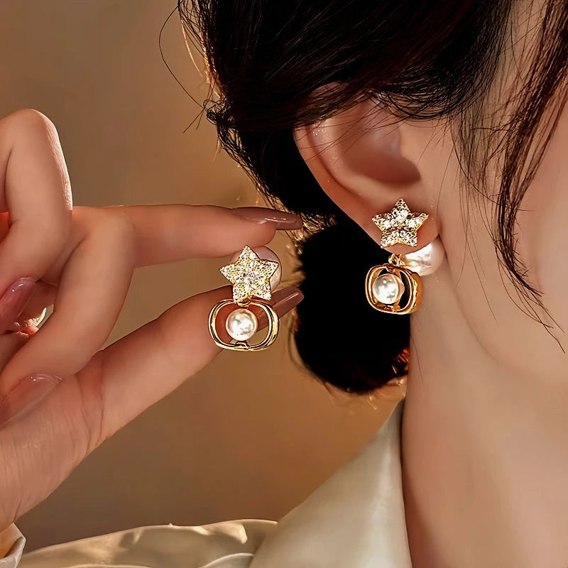 Gold rhinestone star pearl dangle earrings, one worn on ear one held by hand