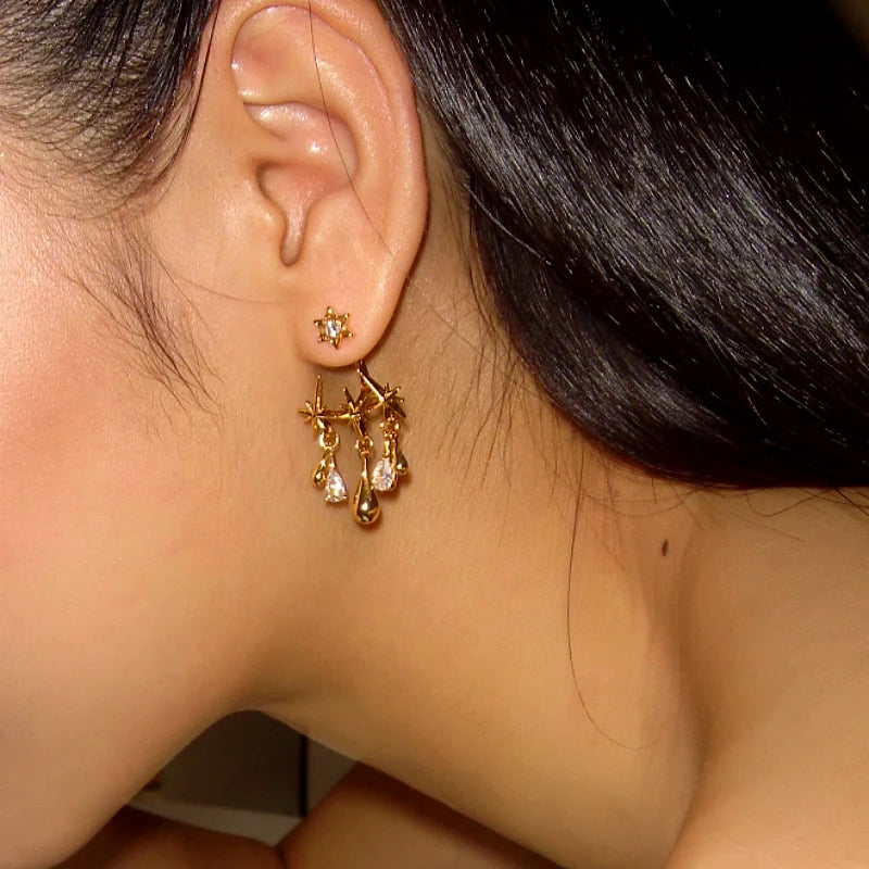 Gold starburst teardrop CZ dangle earrings worn on a model's ear