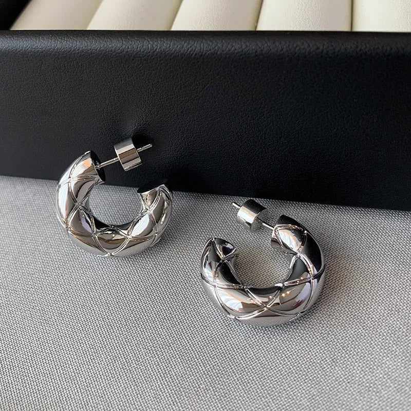 Pair of silver quilted thick C-shaped hoop earrings on gray woven fabric