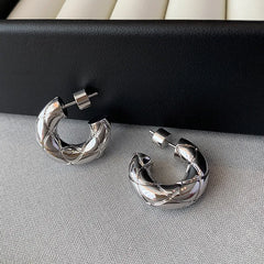 Pair of silver quilted thick C-shaped hoop earrings on gray woven fabric