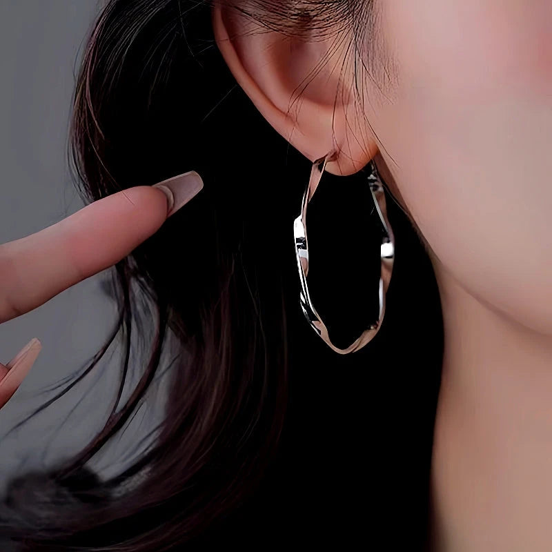 Close-up of silver twisted wavy hoop earring worn on ear